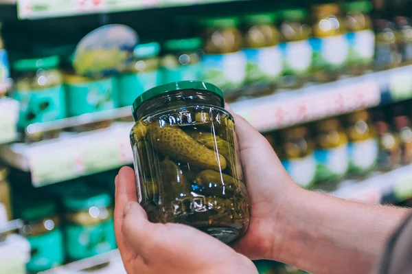 Süpermarketteki adam cam bir salatalık kavanozu tutuyor.