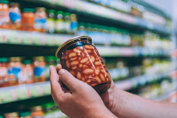 Süpermarketteki adam elinde cam bir kavanoz fasulye tutuyor.