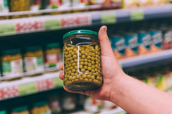 Süpermarketteki adam elinde bezelyeli cam bir kavanoz tutuyor.