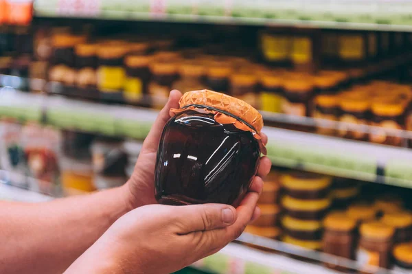 Süpermarketteki adam elinde bir kavanoz bal tutuyor.