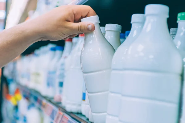 Süpermarkette bir adam vitrinden süt seçiyor.