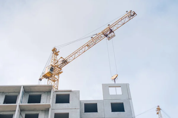 Tower crane for building houses on the background of a panel house and clouds