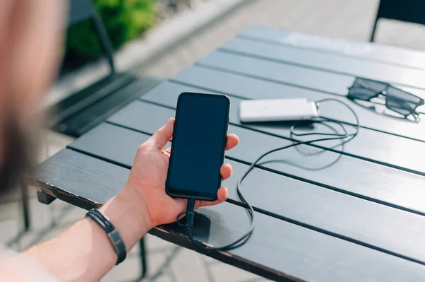 Bir insanın elinde taşınabilir şarj aleti. Powerbank telefonu şarj ediyor
