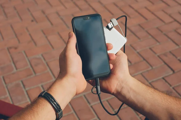 Portable charger in the hands of a person. Powerbank charges the phone