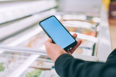 Model teknolojisi. Adam elinde bir akıllı telefon tutuyor. Süpermarketteki vitrinlerin arkasında.