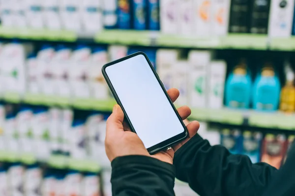 Mock-up technology. The guy holds a smartphone in his hands on the background of showcases in a supermarket