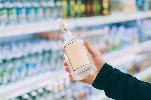 Adam dükkanda bir şişe votka tutuyor.