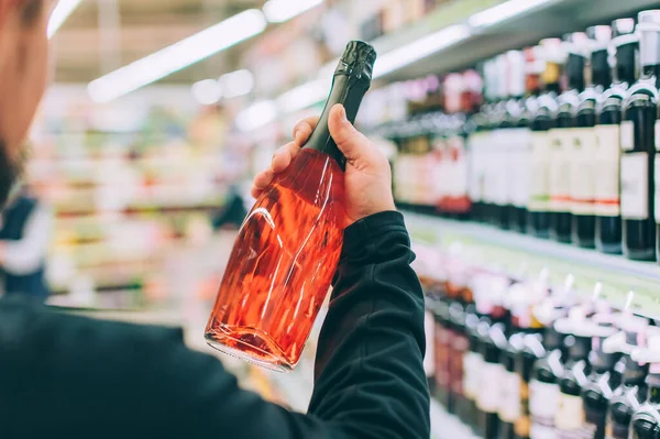 Adam dükkanda bir şişe şarap tutuyor.