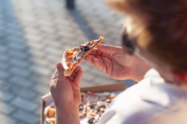 Bir adam elinde bir dilim pizza tutuyor. Temiz havada fast food.