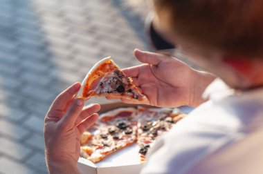 Bir adam elinde bir dilim pizza tutuyor. Temiz havada fast food.