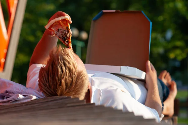 Bankta oturan adam pizza yiyor. Temiz havada fast food.