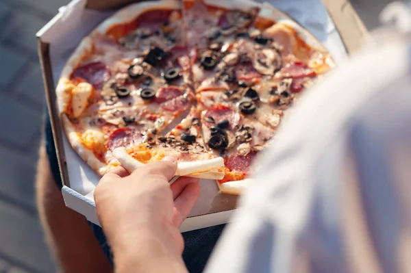 Bir adam elinde bir dilim pizza tutuyor. Temiz havada fast food.