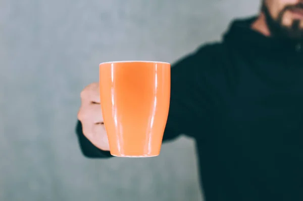 Adam gri bir arka planda elinde turuncu bir bardak tutuyor.