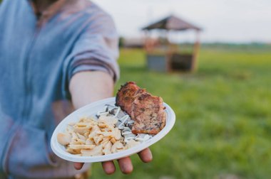 Doğada piknik. Adam elinde mantarlı ve etli bir tabak tutuyor.