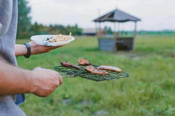 野餐的性质 在大自然的背景下 这家伙手里拿着一盘蘑菇和肉放在烤架上的盘子 — 图库照片