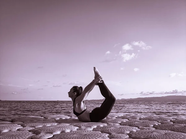 Avrupa görünümlü sportif bir kız deniz kenarındaki bir rıhtımda temiz havada yoga yapıyor.
