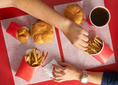 Kırmızı masanın düz manzarası. Elleri yemek seçiyor. Arkadaşları yemek paylaşıyor ve çalıyor.