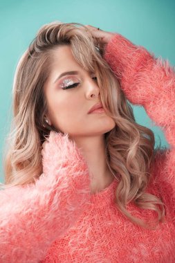 Stüdyo portresi. Güzel, şehvetli, zarif, sarışın, güzel bir kadın. Pastel renkli, pembe kürklü bir süveter giyiyor.