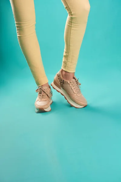 Close up photo of sneakers and yellow skinny jeans against an aqua background in a studio.