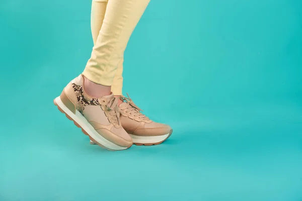 Close up photo of sneakers and yellow skinny jeans against an aqua background in a studio.