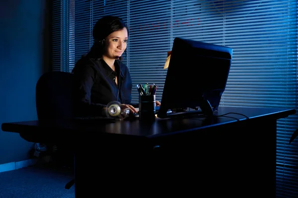 Young latina woman sitting in her room or office working on a computer late or early in the day