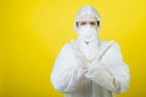scientist girl in a suit for personal protection (PPE) shows the X sign. yellow background