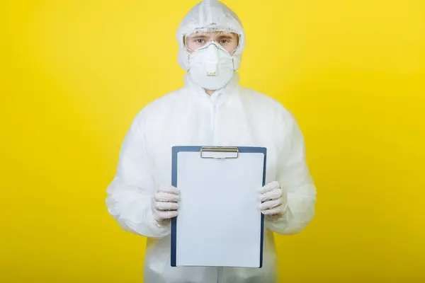 doctor in a suit for personal protection (PPE) with a clipboard on a yellow background