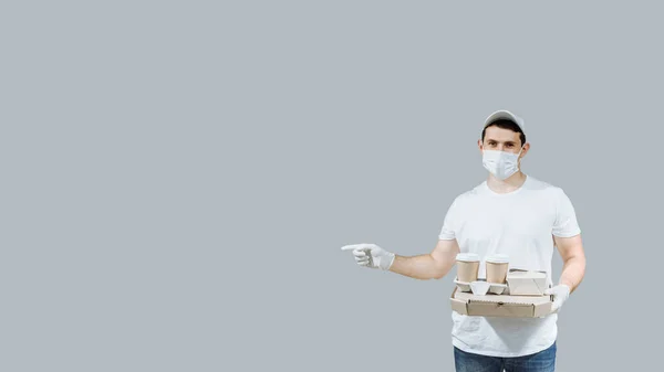 Man courier food delivery man with pizza boxes and coffe shows a finger sign on products isolated on gray background with copy space banner.
