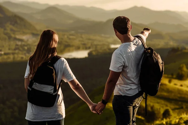 happy couple man and woman enjoy the valley of the mountain and river at sunset. concept of a young family travel with backpacks in the mountain and countryside in nature