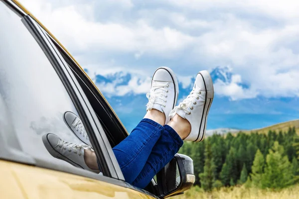 Vacation car trip. Travel and freedom lifestyle concept. Legs of a woman in gumshoes on the background of snowy mountains. Free space