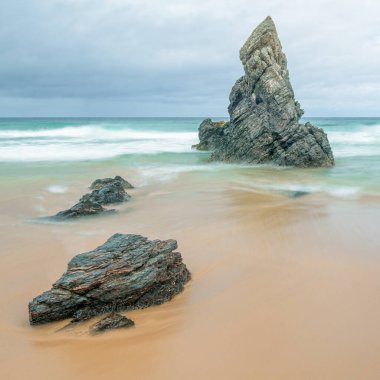 Deniz yığını ve kayalar altın bir plajda, gelgit yaklaşırken