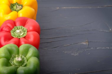 Üç çiğ biber. Üç çiğ biber. Kırmızı, yeşil ve sarı. Koyu gri ahşap arka planda solda. Metin eklemek için alanı olan fotoğraf.