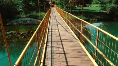 Güneşli bahar gününde dağ nehrinin sakin yeşil sularının üzerinde duran asma köprü.