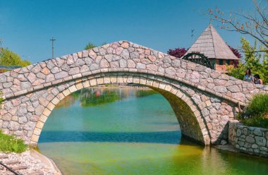 ETHNO VILLAGE STANISICI, BOSNIA VE HERZEGOVINA: 26 Nisan 2018: Bosna-Hersek 'teki Stanisici Etno Köyü' ndeki yeşil su üzerindeki taş köprü.