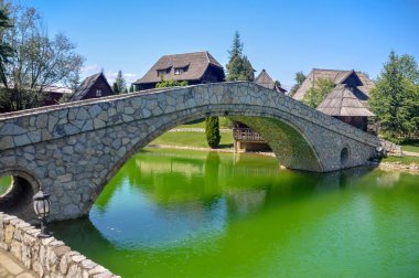 ETHNO VILLAGE STANISICI, BOSNIA VE HERZEGOVINA: 26 Nisan 2018: Bosna-Hersek 'teki Stanisici Etno Köyü' ndeki yeşil su üzerindeki taş köprü.
