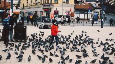 SARAJEVO, BOSNIA VE HERZEGOVINA, 26 Şubat 2019: Kestane adam ve Bosna-Hersek 'in başkenti Saraybosna' daki Bascarsija 'da bir barmenle birlikte güvercinlerin arasında genç bir çocuk.