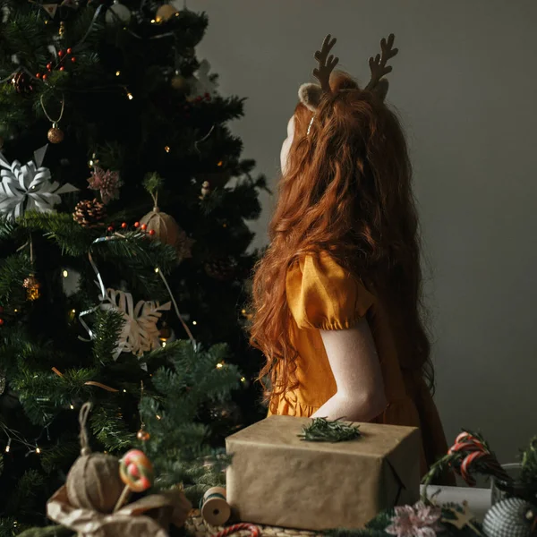 赤毛の女の子見ますAクリスマスツリースタンドでテーブルの上にギフト — ストック写真