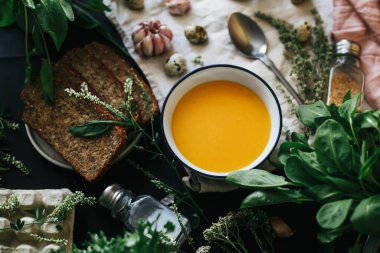 Ekmekli bir porsiyon sıcak balkabağı çorbası koyu bir masa örtüsü üzerinde servis edilir..