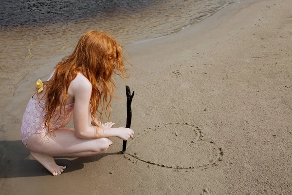 Рыжая Девушка Купальнике Рисует Песке Палкой — стоковое фото