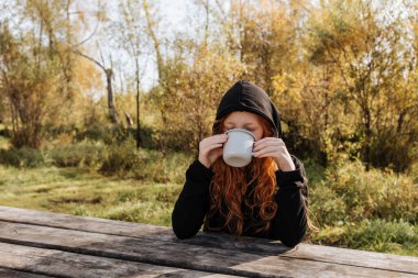 Sonbahar pikniğinde kızıl saçlı kız bir kupadan çay içiyor.