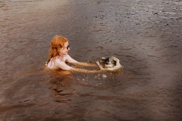 Rudowłosa Dziewczyna Uczy Swojego Mopsa Pływać Rzece — Zdjęcie stockowe