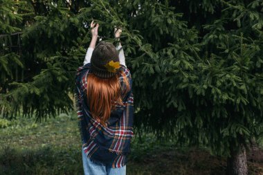 Düşmüş yapraklarla süslenmiş örülmüş şapkalı kızıl saçlı kız..
