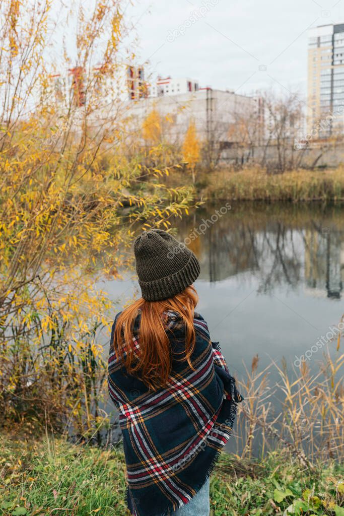 Redhead girl in knitted hat enjoying lake view on warm autumn day.