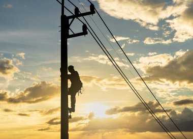 Siluet adam elektrik direğinde çalışıyor. Gün batımı gökyüzünde..