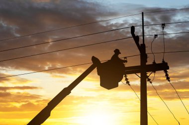 Silüet elektrikçi yüksek voltaj iletim hatlarını korumak için teleferik üzerinde çalışıyor..