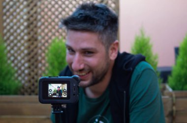 Sosyal medya etkileyicisi içerik yaratmak için kamera kullanıyor. Adam dışarıda kendini videoya çekiyor.