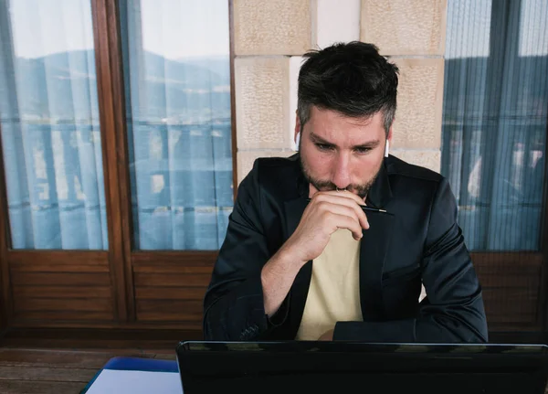 Middle-aged businessman working from home using a laptop, headphones and a notebook on the terrace