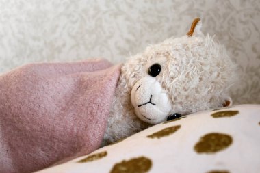 Çocuk odasında sevimli bir oyuncak. Yorganın altında, yatağın üstünde pelüş bir koyun.