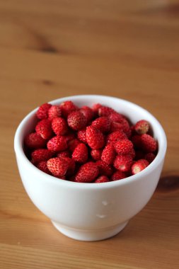 Kasede küçük kırmızı böğürtlen. Tahta masada beyaz kasede yabani çilek..
