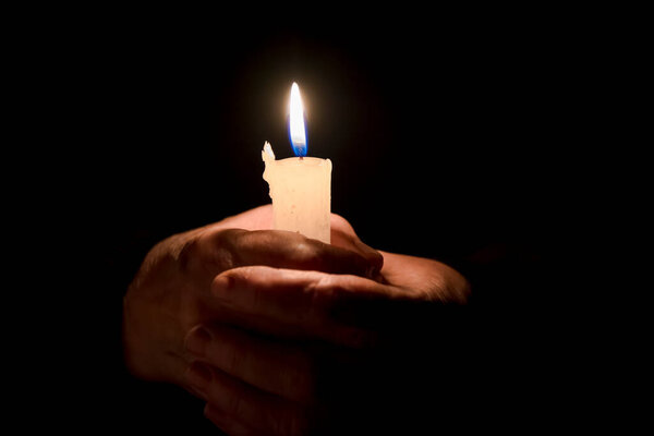 old man's hands hold a burning candle of memory and sorrow